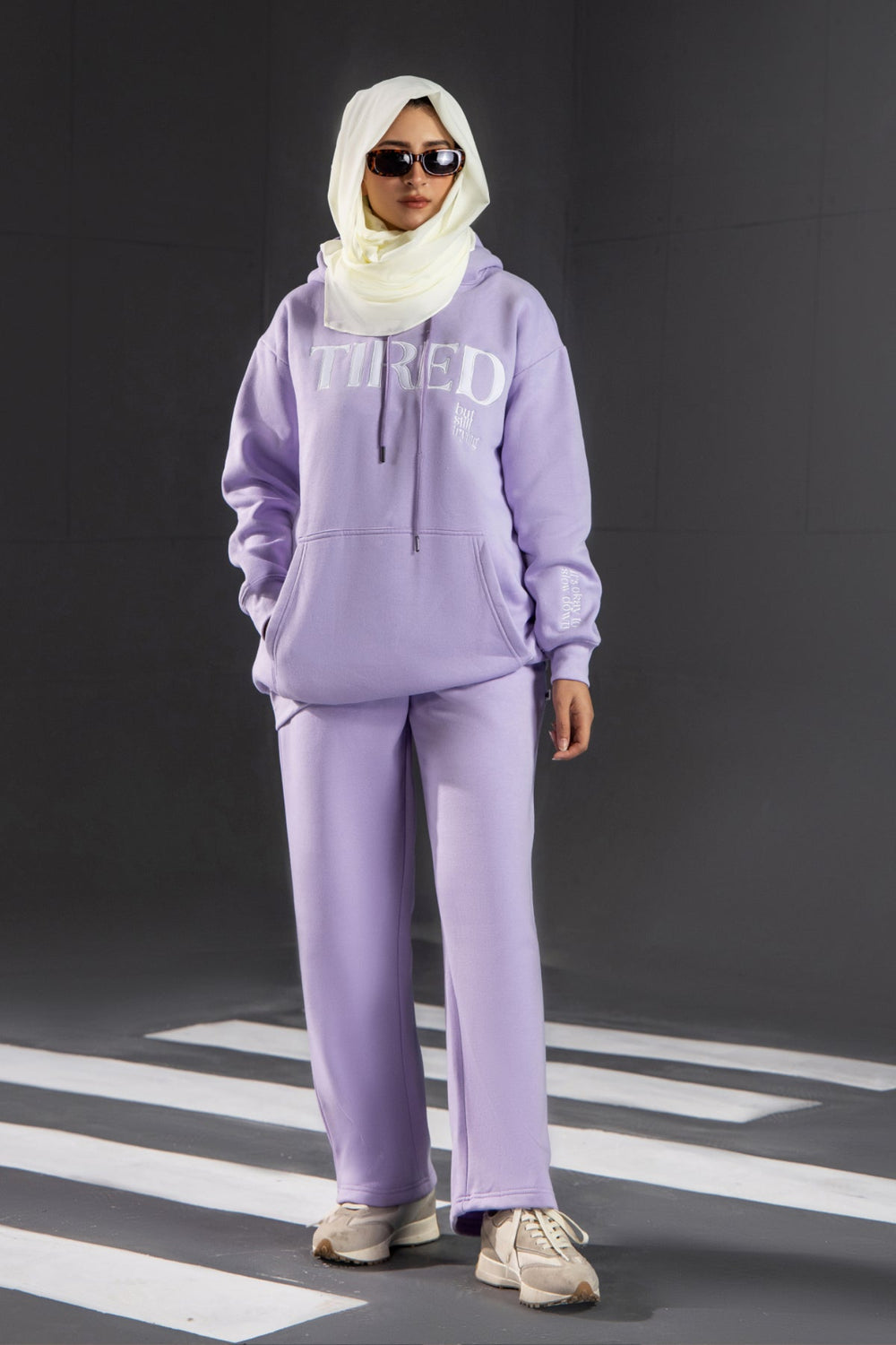 Person wearing a lavender tracksuit with 'TIRED' text on a black background