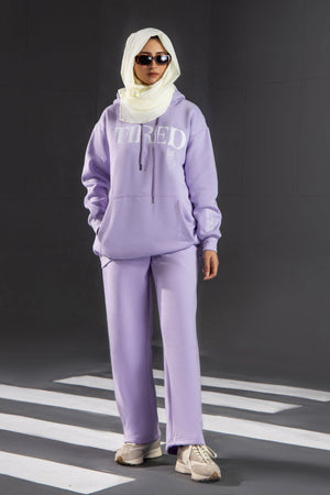 Person wearing a lavender tracksuit with 'TIRED' text on a black background